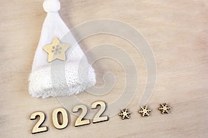 New year number 2022 lined with wooden figures on the wooden surface next to the white Christmas hat