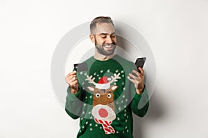 New Year, online shopping and christmas concept. Handsome caucasian man paying in internet, holding smartphone and