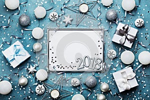 New year 2018 party background. Silver frame with christmas decoration, gift box, confetti and sequins on vintage blue table.