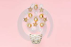 New Year party festive background - golden glossy and sparkling balls, ribbon, stars, snowflakes flying above bowl on pastel pink.