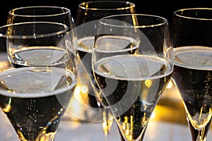 New year party, small bubbles of brut champagne cava or prosecco wine in tulip glasses with garland lights on background