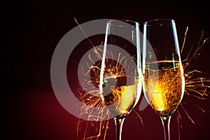 New Year party time with two champagne glasses and sparklers against a dark red background, copy space