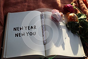 New year personal notes on a notebook with wilted roses and a pen on the table. Motivational note a book - New Year, New You.