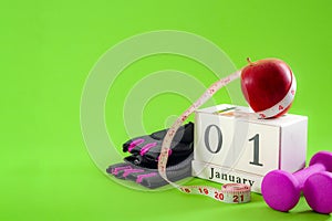 New year resolution and start a diet concept with an apple, pink dumbbells and gym gloves next to a cube calendar showing the date