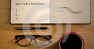 New year resolutions in book with spectacles, coffee mug and pen on table