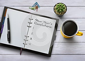 New Year resolutions, goals or action plan concept. Notebook on white wooden table with coffee, plant and stationery. Flat lay