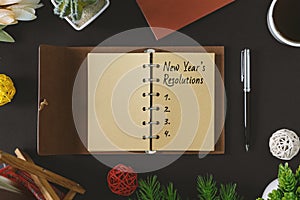 New Year Resolutions text on rustic notepad with pen and coffee on black background.