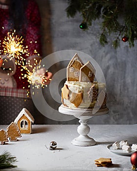 New Year`s cake on a stand with gingerbread, houses, stars and Christmas trees, hands are holding sparklers