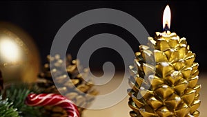 A New Year\'s candle in the shape of a golden cone burns on a festive table next to Christmas decorations