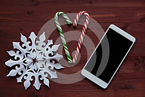 New Year`s Christmas concept. Snowflake made of paper, lollipops and a smartphone on a wooden table