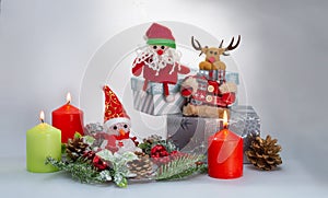 New year`s composition: a toy Santa Claus, a reindeer and a Snowman, burning colored candles and gifts