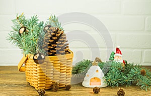 New Year`s composition on a wooden table near a white brick wall wicker basket with spruce branches, balls, cedar cone. lit candl