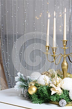 New Year& x27;s decorations and a golden candlestick with burning candles stand on the surface of a white grand piano