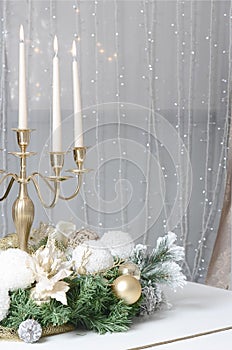 New Year`s decorations and a golden candlestick with burning candles stand on the surface of a white grand piano