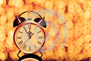 New year`s eve midnight. Retro alarm clock whose pointer shows five to twelve on festive bokeh background