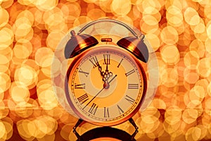 New year`s eve midnight. Retro alarm clock whose pointer shows five to twelve on festive bokeh background