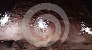 A New Year's fireworks display is lit, standing in the snow. Sparklers