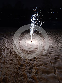 A New Year's fireworks display is lit, standing in the snow. Sparklers
