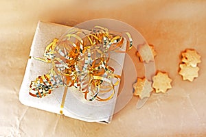 New Year`s gift wrapped in craft paper with a gold ribbon and Christmas cookies, congratulations