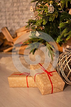 New year`s gifts and wicker basket under beautiful Christmas-tree with fireplace hearth and grey brick wall background.