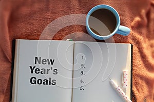 New year`s goals concept. New year`s resolutions. With a cup of morning coffee, book and a pen on the table. New year`s plans.