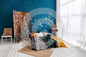 New Year`s interior with a bed and a Christmas tree in a bright room.