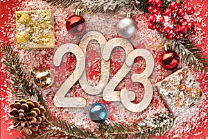 New Year's number 2023 made of wooden numbers on red paper with Christmas balls, gift boxes, fir branches