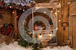 New Year`s photo zone with snow near a wooden house. Christmas decor: toys, Christmas trees, skis, garland, firewood, glowing