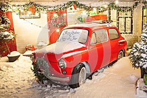 New Year`s red car in the snow on the background of the house and with a Christmas tree