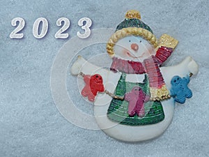 New Year\'s snowman on the background of white snow and the numbers of the new year 2023.