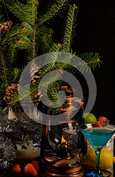 New year`s still life. On a dark background, branches of a fir tree in a large vase next to an old kerosene lamp