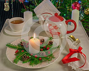 New Year's tea party at the table with a teapot, candles on the background of the Christmas tree