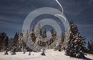 New Year's trail from a star in the night sky as a background for snow-covered trees in a beautiful valley