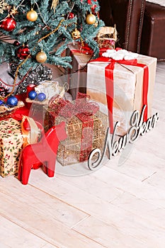 The New Year`s tree decorated with spheres and a garland, gifts, the inscription `New Year` and a red figurine of a horse