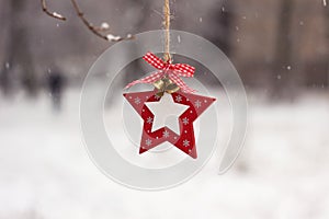 New Year`s white-red toy in the form of a star hangs on a tree on the street in winter in snowy weather. Christmas concept