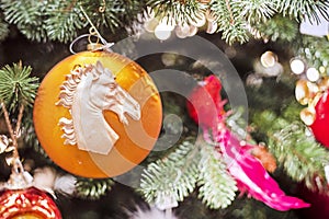 New Year\'s yellow ball with a bust of a horse hangs on a branch of a Christmas tree.