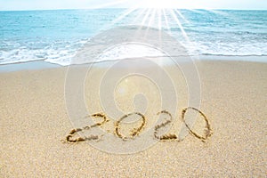 New Year 2020 on the sandy shore against the backdrop of sea waves. Beautiful sunrays illuminate the inscription 2020 on the sand