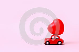 New Year . Small red retro toy car with heart on the roof on pink background . Christmas, Valentines Day, World Womans Day