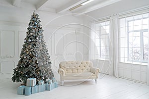 New Year studio interior. Christmas tree is decorated with balloons, with Christmas gifts under it. White sofa stands