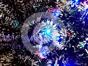 New Year tinsel with neon lights on a Christmas tree closeup