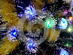 New Year tinsel with neon lights on a Christmas tree closeup