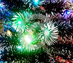 New Year tinsel with neon lights on a Christmas tree closeup