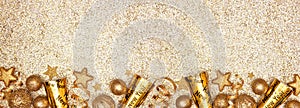 New Years Eve border banner of gold decorations, steamers and noisemakers, above view over a glittery gold background