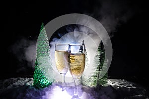 New Years Eve celebration background with pair of flutes and bottle of champagne with christmas tree on snow on dark background.