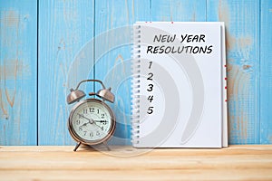 New years Resolutions text on notebook and retro alarm clock on table and copy space.