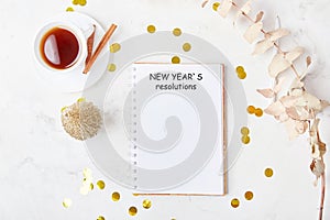 New Years resolutions text on white mock up notebook on the festive desk with coffee cup