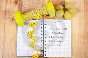 New years resolutions written in notebook and dumbbells with centimeter