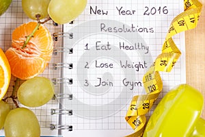 New years resolutions written in notebook and fruits, dumbbells with centimeter