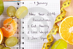 New years resolutions written in notebook and fruits, dumbbells with centimeter