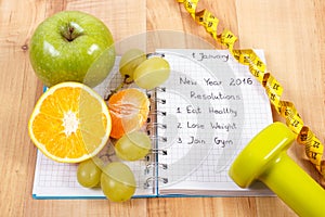 New years resolutions written in notebook and fruits, dumbbells with centimeter